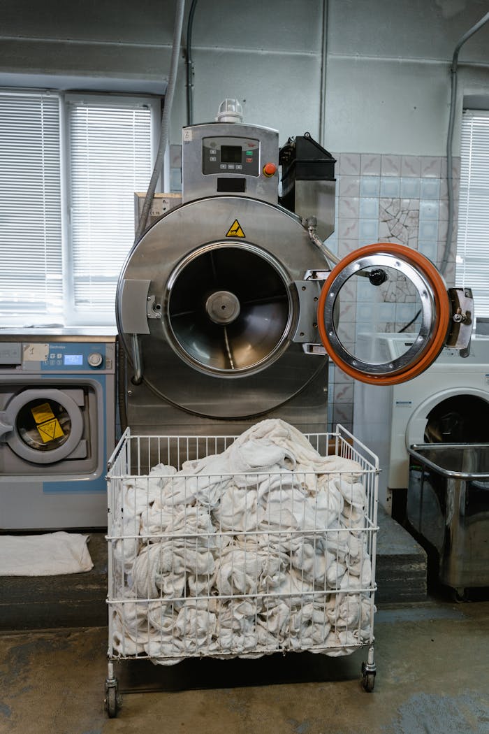 Large industrial washing machine with a cart full of linens in a laundry facility.